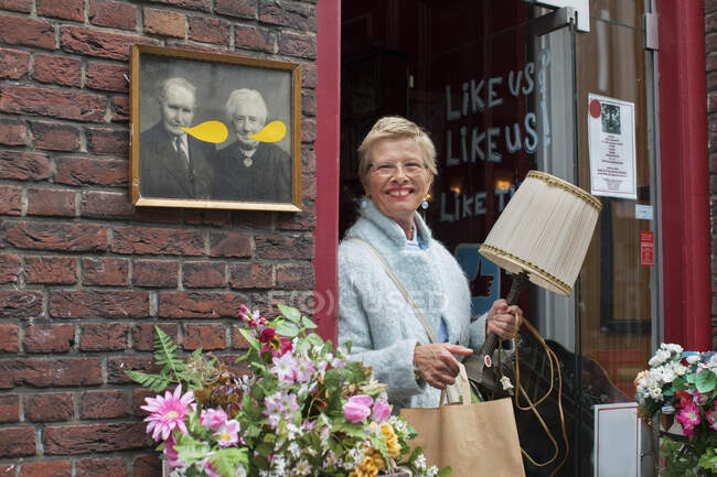 Зріла жінка-клієнт несе лампу і сумку за межами старовинного магазину — стокове фото