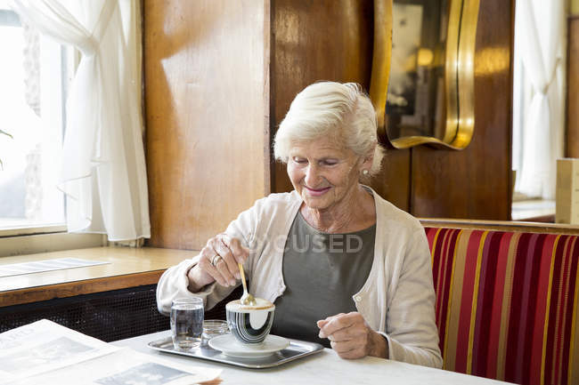 Senior mulher sentada no café, mexendo café — Fotografia de Stock