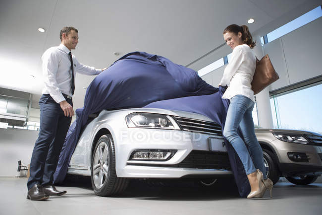 Salesman uncovering new car to female customer in car dealership — Stock Photo