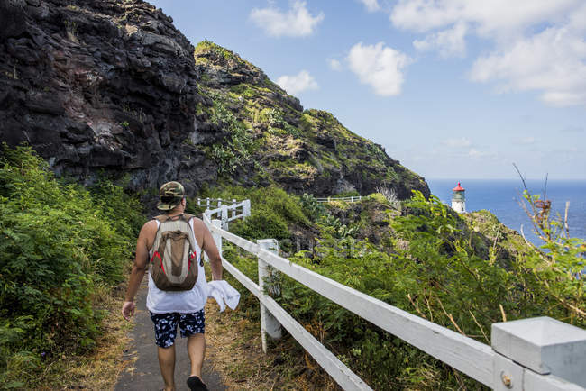 Vista trasera del joven turista masculino caminando hacia el faro de Makapuu, Oahu, Hawaii, EE.UU. - foto de stock