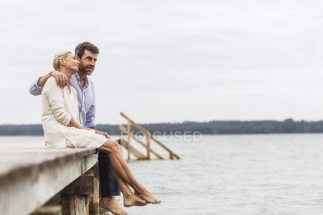Зріла пара сидить на краю пірсу, розслабляючись — стокове фото