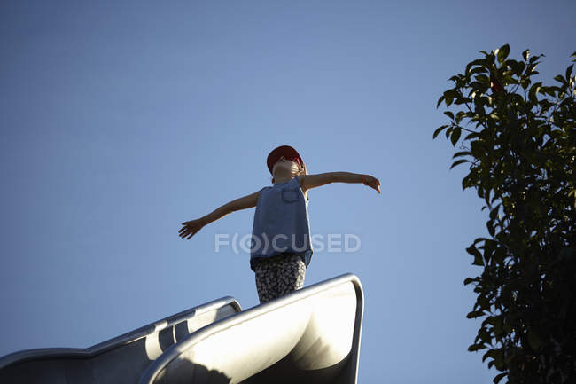 Девушка, стоящая с распростертыми объятиями на вершине горки парка — стоковое фото