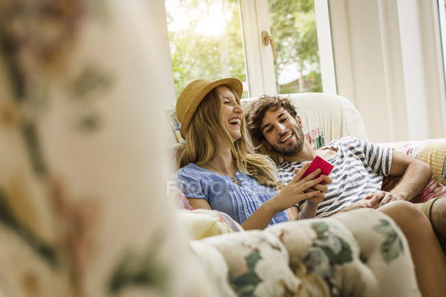 Jovem casal leitura mensagem no smartphone na sala de estar — Fotografia de Stock