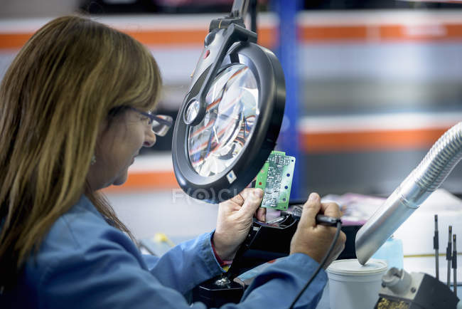 Female worker soldering electronic parts in clean room in electronics factory — Stock Photo