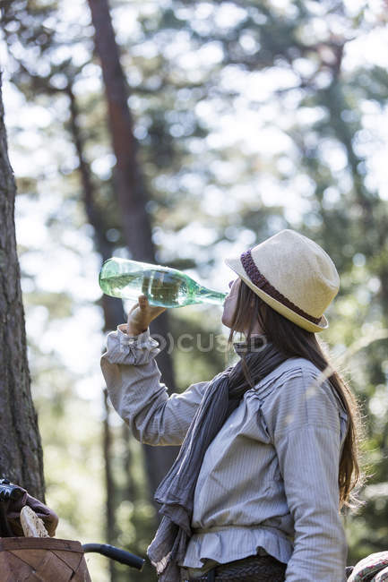 Зріла жінка велосипедист п'є з пляшки води в лісі — стокове фото