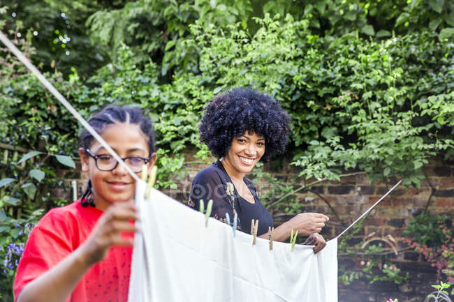 Boy and mother pegging sheets on garden clothesline — Stock Photo