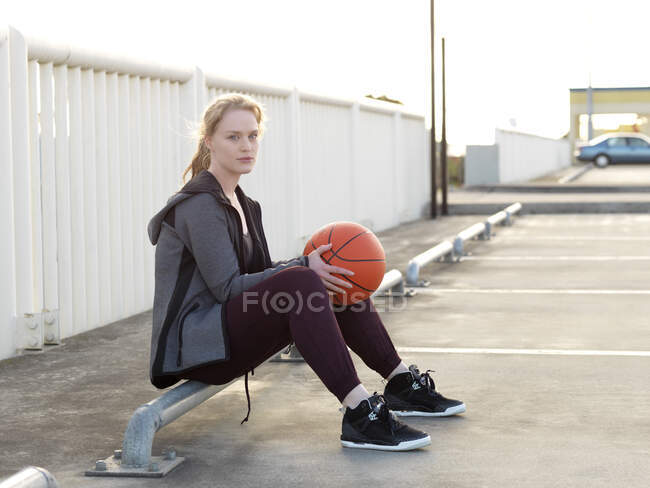 Young female basketball player sitting in parking lot — Stock Photo