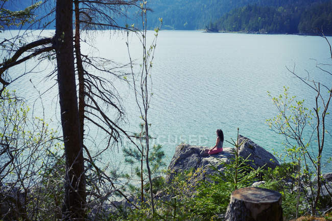 Середня доросла жінка, сидить на скелі, в положенні йоги, вид ззаду — стокове фото