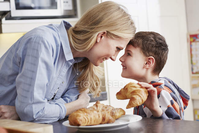 Niño sosteniendo croissant, cara a cara con la madre - foto de stock