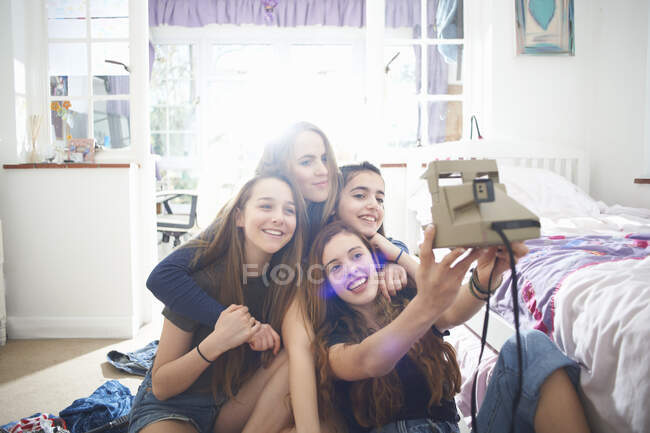 Four teenage girls taking instant camera selfie in bedroom — Stock Photo
