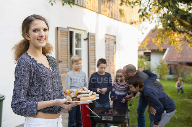 Portrait of teenage girl carrying plate of barbecued food at garden barbecue — Stock Photo