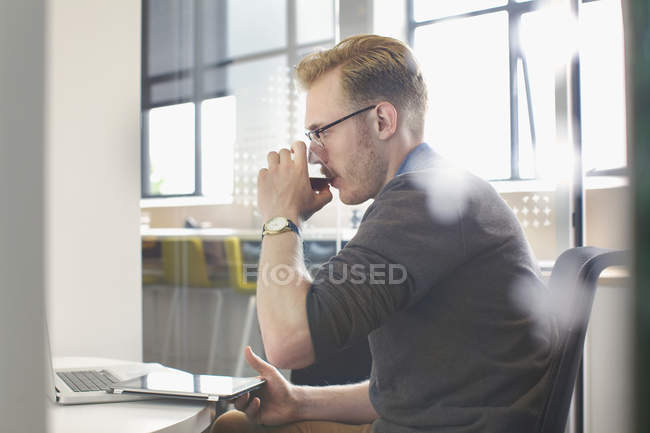 Young man drinking coffee at office desk — Stock Photo