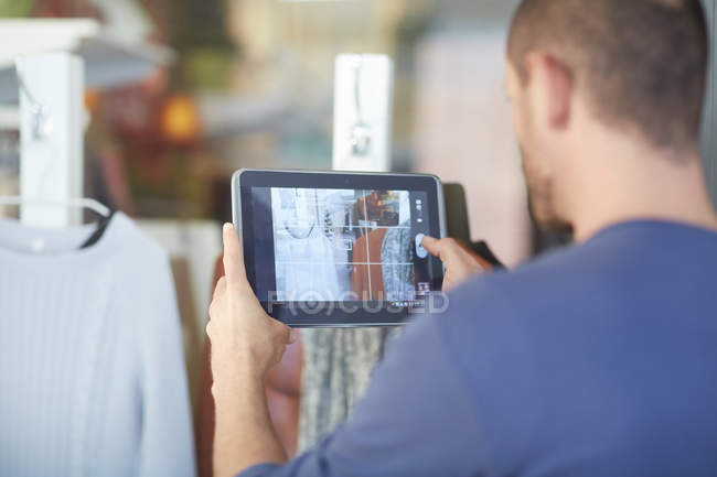 Mid adult man holding digital tablet, taking photograph of shop window — Stock Photo