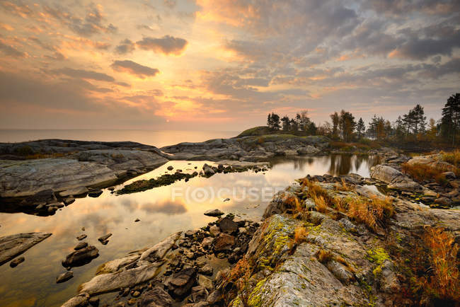 Felsen am Seeufer und Sonnenuntergang bewölkter Himmel, der sich im Wasser spiegelt — Stockfoto