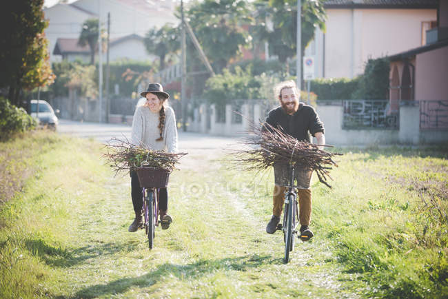 Pareja joven llevando racimos de palos en bicicletas - foto de stock