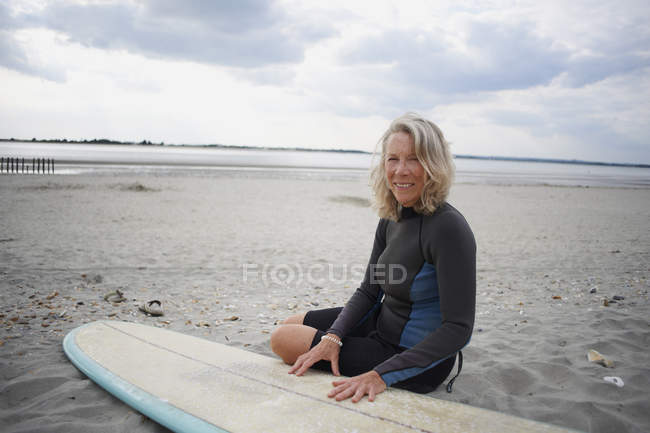 Портрет пожилой женщины, сидящей на пляже рядом с доской для серфинга — стоковое фото
