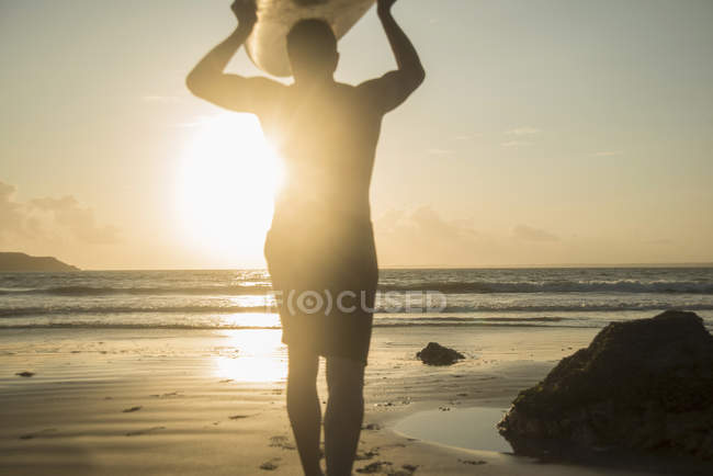 Silhouette eines Mannes, der auf das Meer zugeht und ein Surfbrett hält — Stockfoto