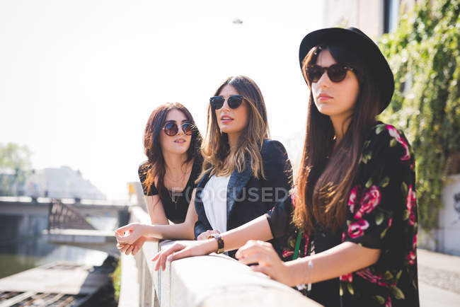 Три стильные молодые подруги, выглядывающие из города на берег реки — стоковое фото