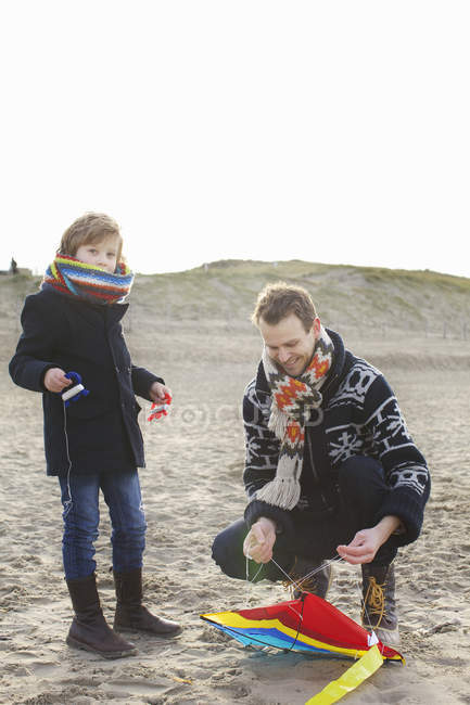 Hombre adulto medio preparando cometa para su hijo en la playa, Bloemendaal aan Zee, Países Bajos - foto de stock