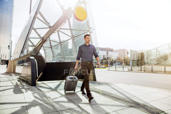 Homme d'affaires avec valise à roues marchant par escalator — Photo de stock