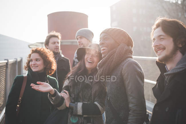 Six jeunes amis adultes bavardant et riant sur la passerelle — Photo de stock
