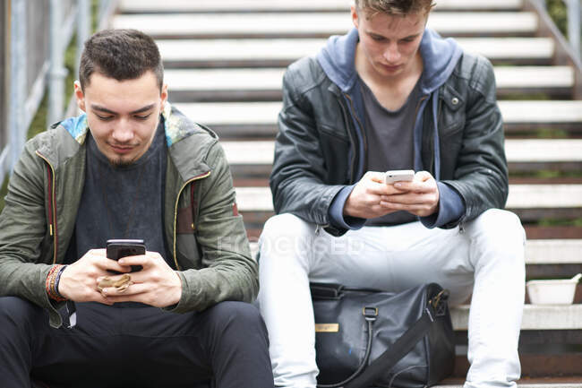 Dois jovens, sentados em degraus, usando smartphones, ao ar livre — Fotografia de Stock