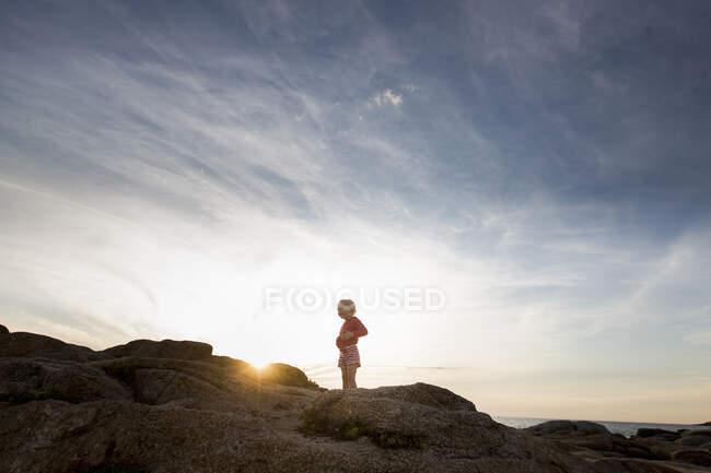 Petite fille silhouettée sur un rocher côtier au coucher du soleil, Calvi, Corse, France — Photo de stock