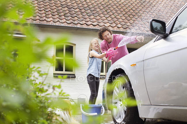 Girl helping father washing car by building in countryside — Stock Photo
