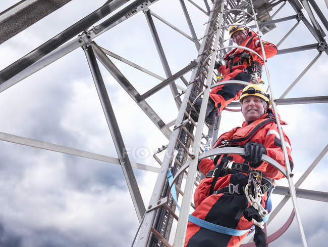 Retrato de los trabajadores de la torre escalando la torre de radio en el parque eólico en alta mar, vista de ángulo bajo - foto de stock