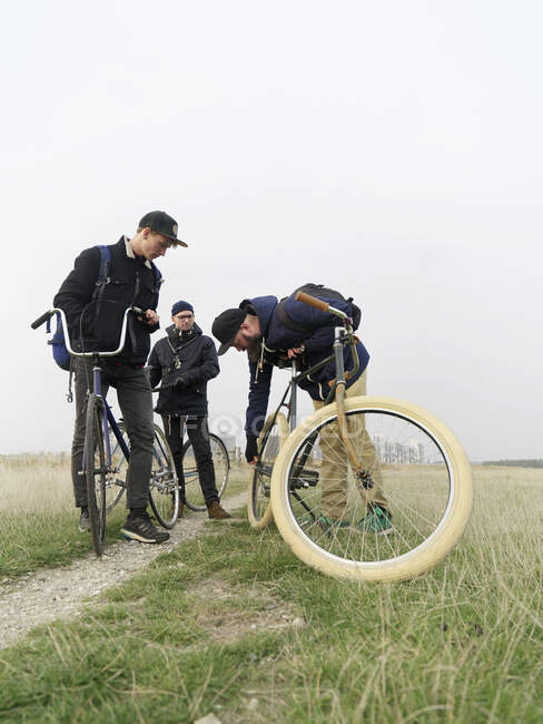 Urban cyclists checking tyre in field — Stock Photo