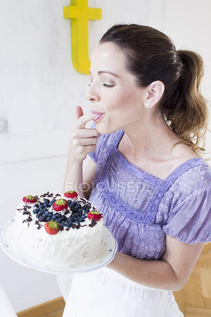 Mature woman holding cake and licking finger — Stock Photo