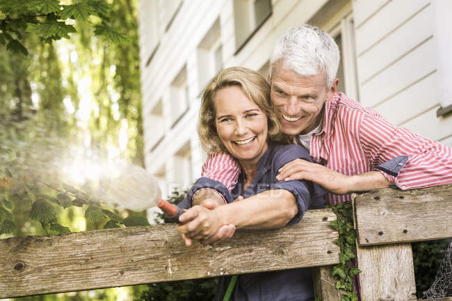 Esposo y esposa jugando con la manguera en el jardín - foto de stock