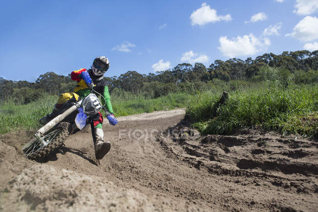 Jovem masculino motocross piloto de corrida através de lama pista curva — Fotografia de Stock