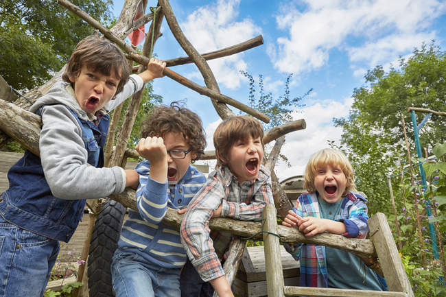 Quatre garçons criant sur le cadre d'escalade fait maison dans le jardin — Photo de stock