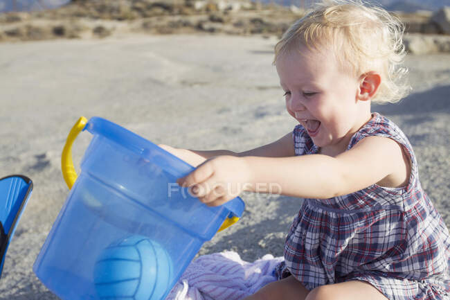 Счастливая девочка, играющая на пляже с игрушечным ведром — стоковое фото