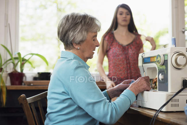 Senior woman using sewing machine with granddaughter at home — Stock Photo