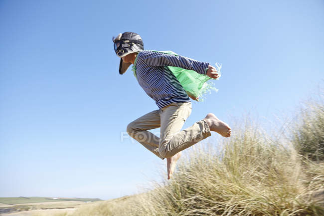 Молодий хлопчик на пляжі, одягнений у вишукане плаття, прикидається літаючим — стокове фото