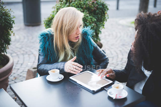 Deux jeunes femmes utilisant une tablette numérique au café sur le trottoir — Photo de stock