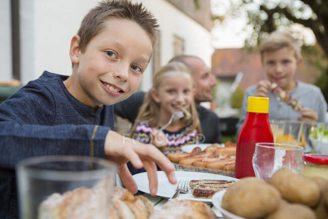 Portrait de garçon et de famille à la table de barbecue du jardin — Photo de stock