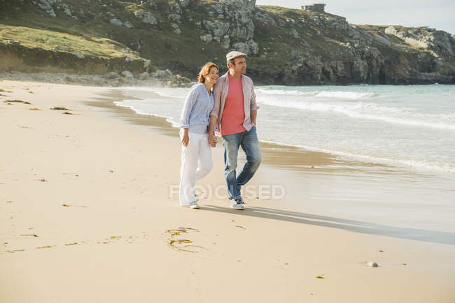 Зрелая пара, держащаяся за руки, прогуливаясь по пляжу, Камаре-сюр-мер, Бретань, Франция — стоковое фото
