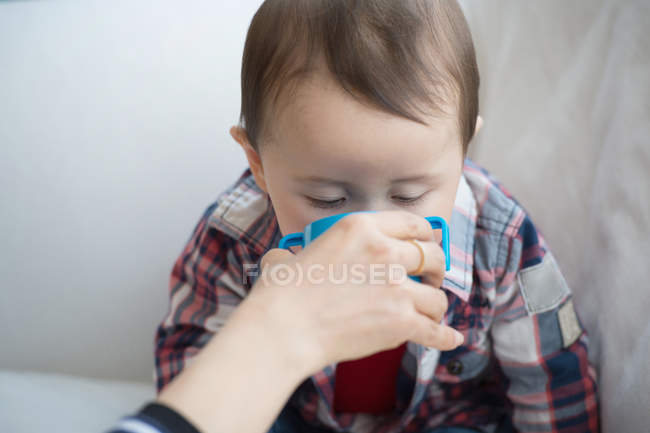 Mãe ajudando bebê menino bebida de copo — Fotografia de Stock
