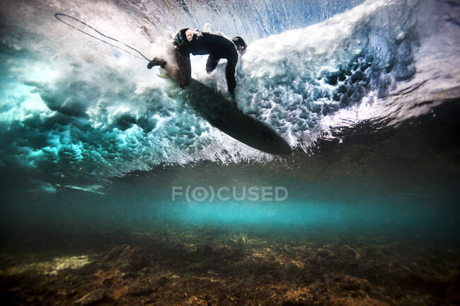Vista submarina del surfista cayendo a través del agua después de atrapar una ola en un arrecife poco profundo en Bali, Indonesia - foto de stock
