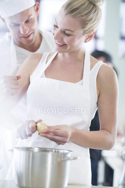 Chef y colega pelando papas en cocina comercial - foto de stock