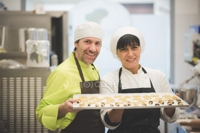 Cozinheiros que transportam bandeja de doces em cozinha comercial — Fotografia de Stock
