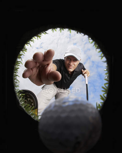 Vista attraverso il foro del golfista che raggiunge per la palla da golf — Foto stock