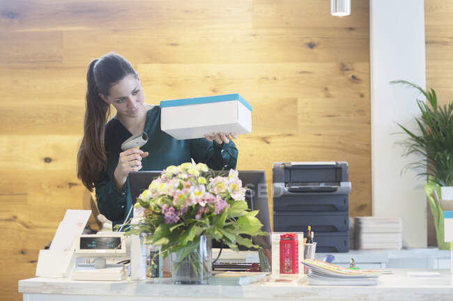 Assistante de vente féminine utilisant un lecteur de code à barres sur une boîte à chaussures — Photo de stock