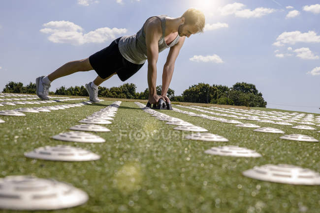 Young man doing push ups with hand weights on sports field — Stock Photo
