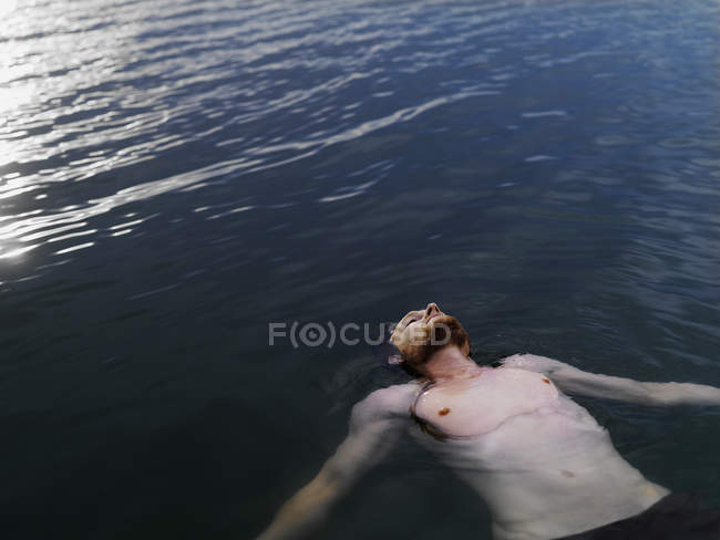 Високий кут зору молодого чоловіка, який плаває на спині у водяних обіймах, простягнутий, дивлячись вгору — стокове фото