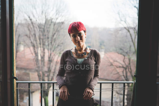 Молода жінка, спираючись на балконні перила, посміхається — стокове фото