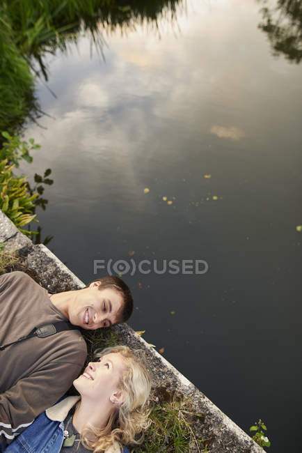 Overhead view of young couple lying on river footbridge — Stock Photo
